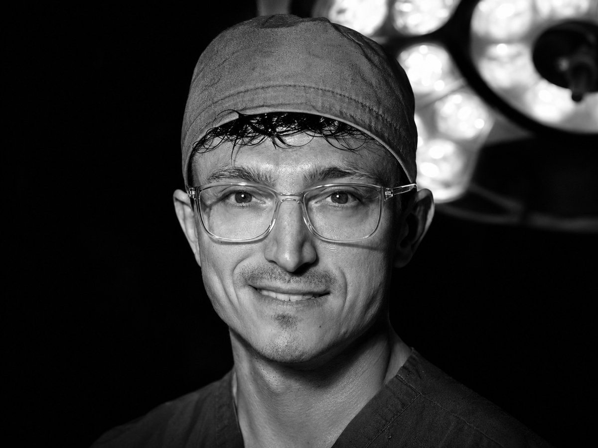 Black and white portrait of Dr. Andre Rafizadeh in surgical cap and glasses under operating room lights